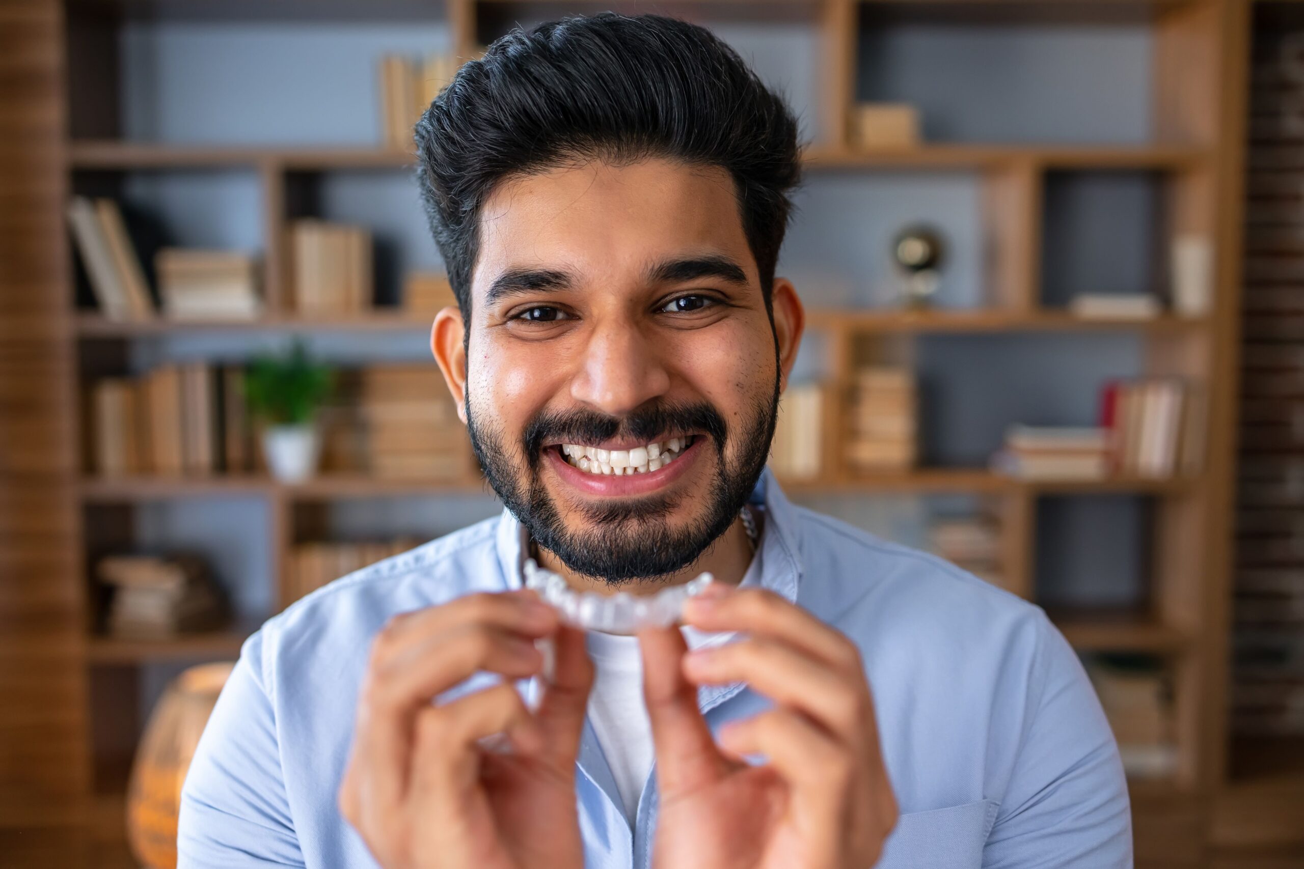 Smiling man holding a clear dental aligner