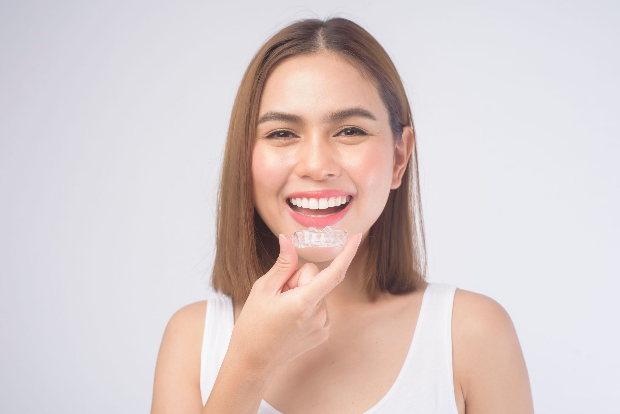 Woman smiling while wearing a clear dental aligner